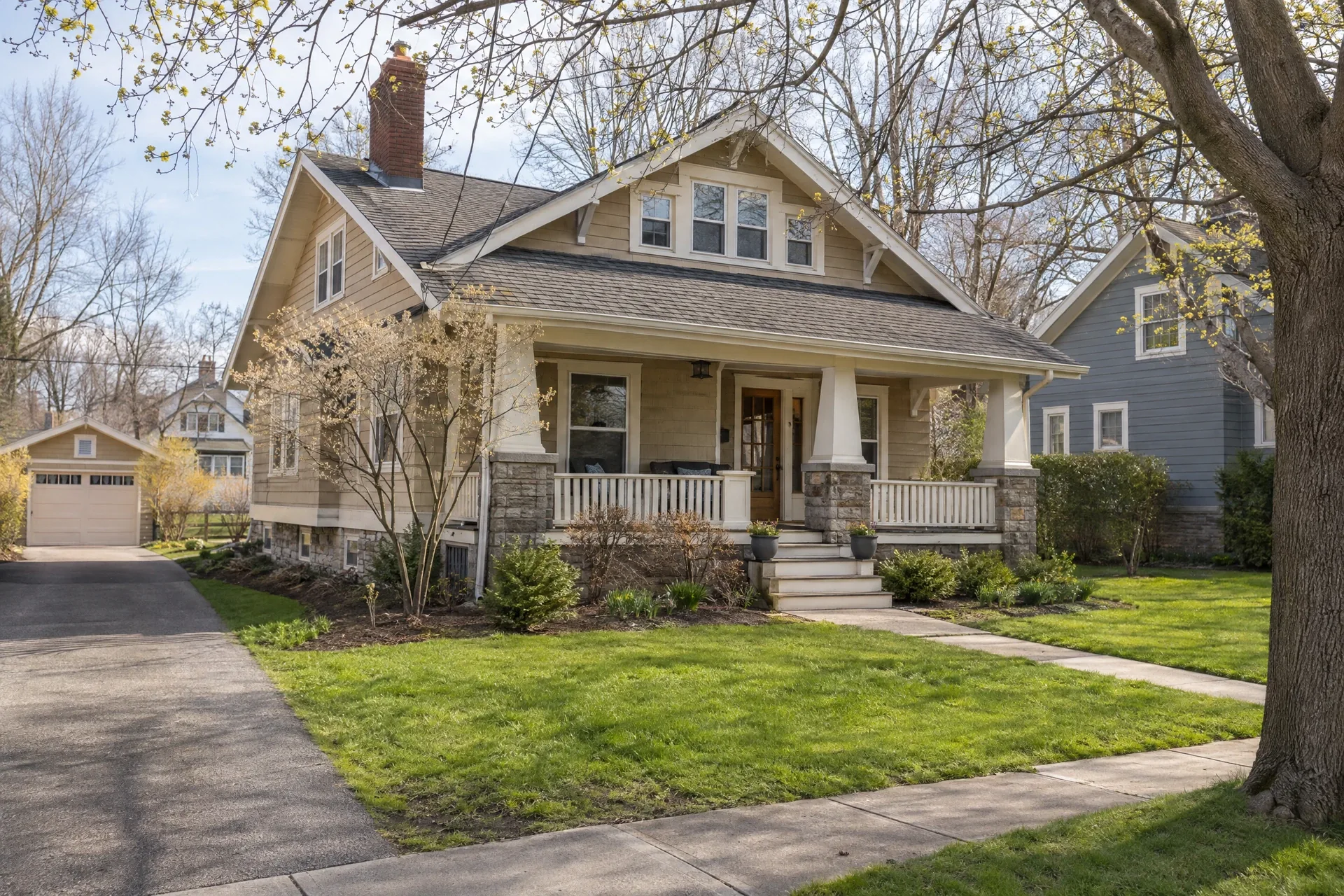 Tan Craftsman bungalow with covered porch, front path and spring trees