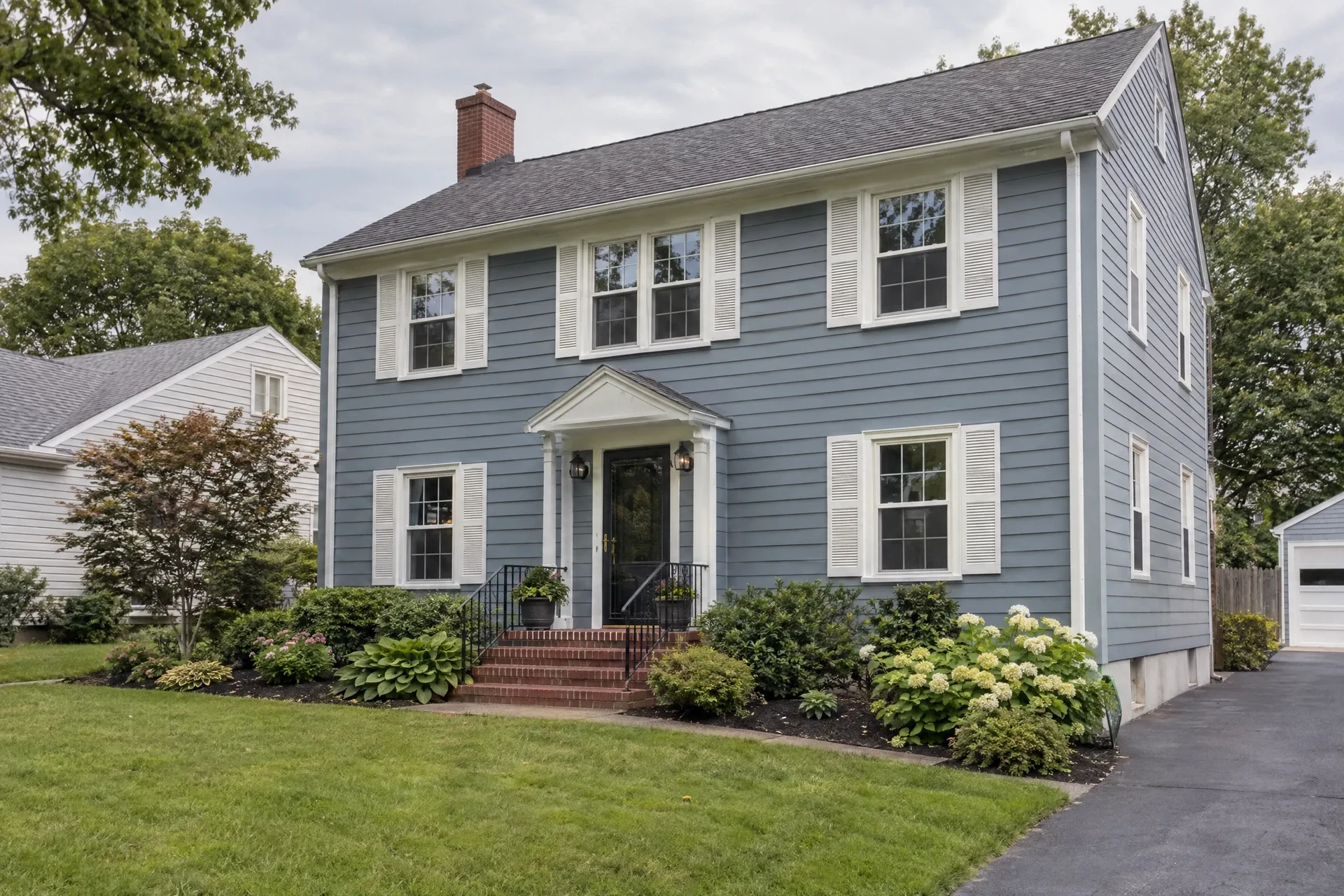 Muted-blue Colonial home with white shutters, brick stoop and a tidy garden